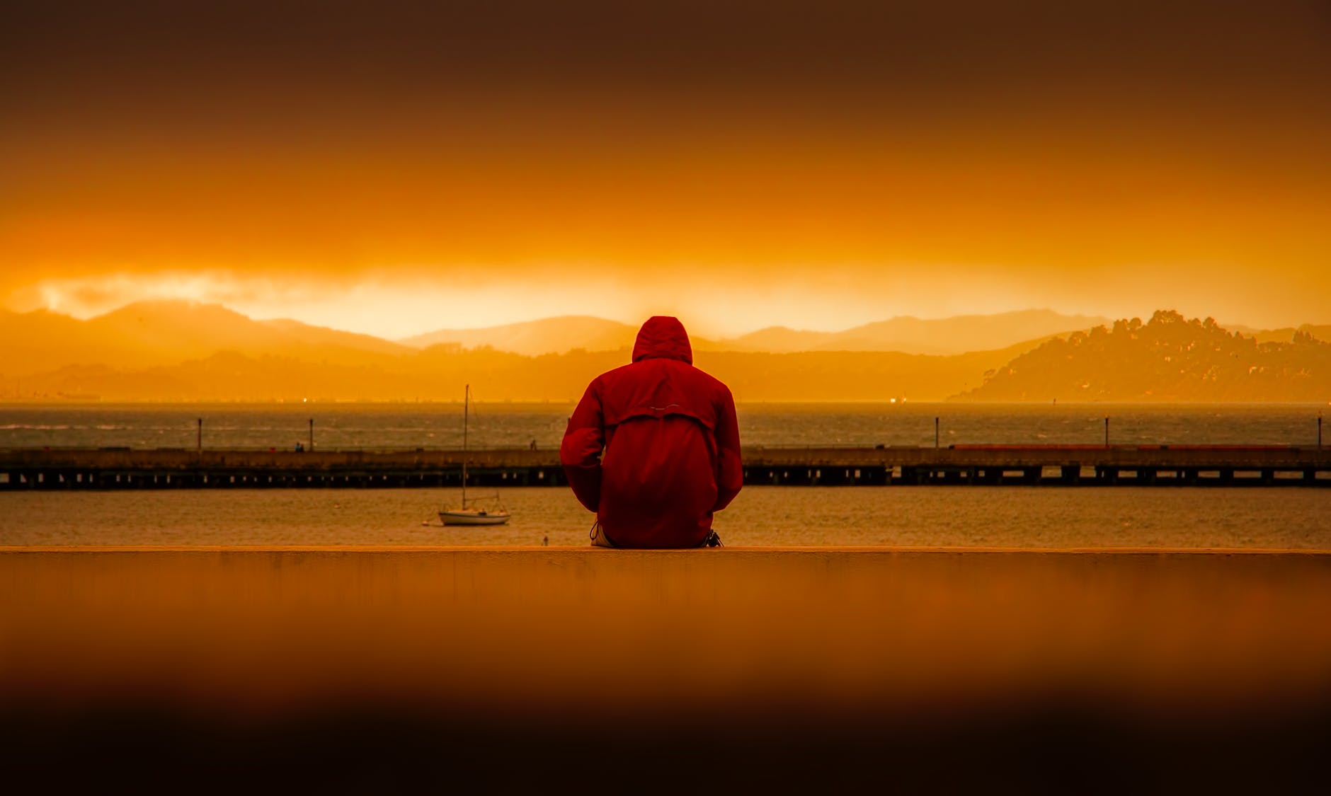 person wearing red hoodie sitting in front of body of water tristeza e depressão