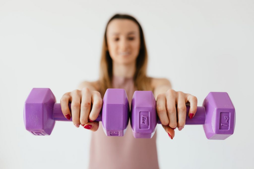 purple dumbbells in hands of positive sportswoman