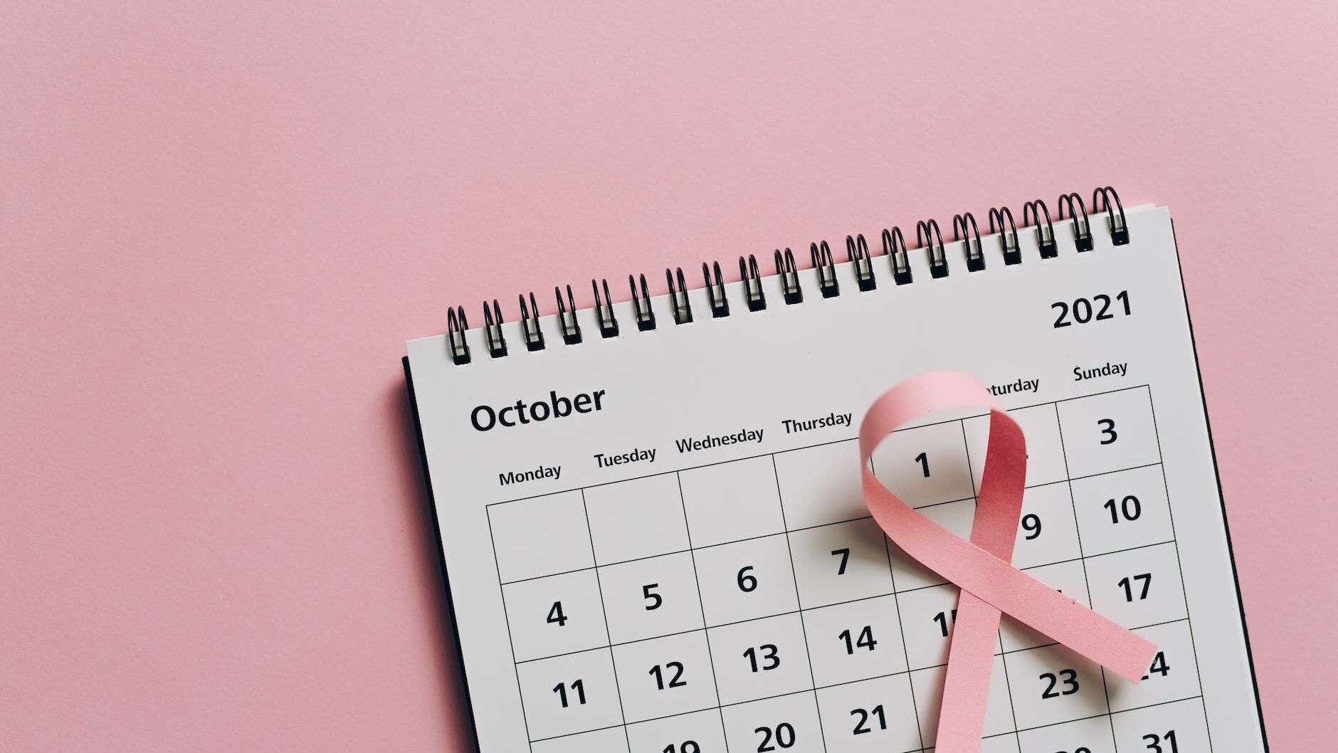 close up shot of a pink ribbon on a calendar câncer de mama e outubro rosa
